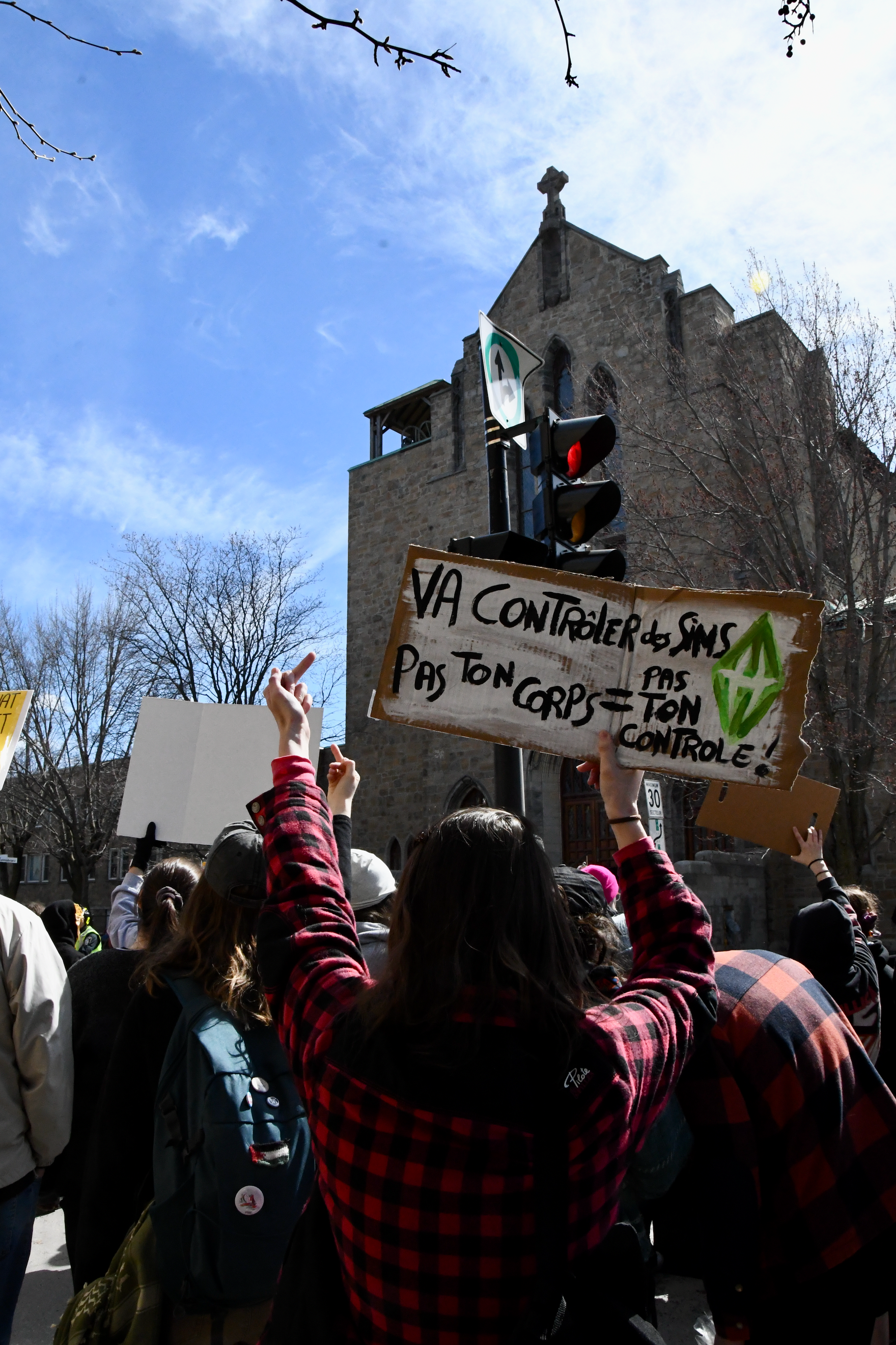 Devant une église évangélique, des manifestant'es pro-choix dénoncent un évènement anti-choix à l'église. Une personne tient une pancarte où est écrit: «va contrôler des Sims; pas ton cops = pas ton contrôle! »